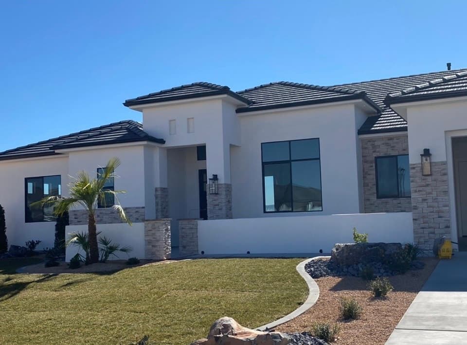 Single-story home with bright white stucco, a dark tile roof, and light stone veneer at the entry pilasters and garage-side wall
